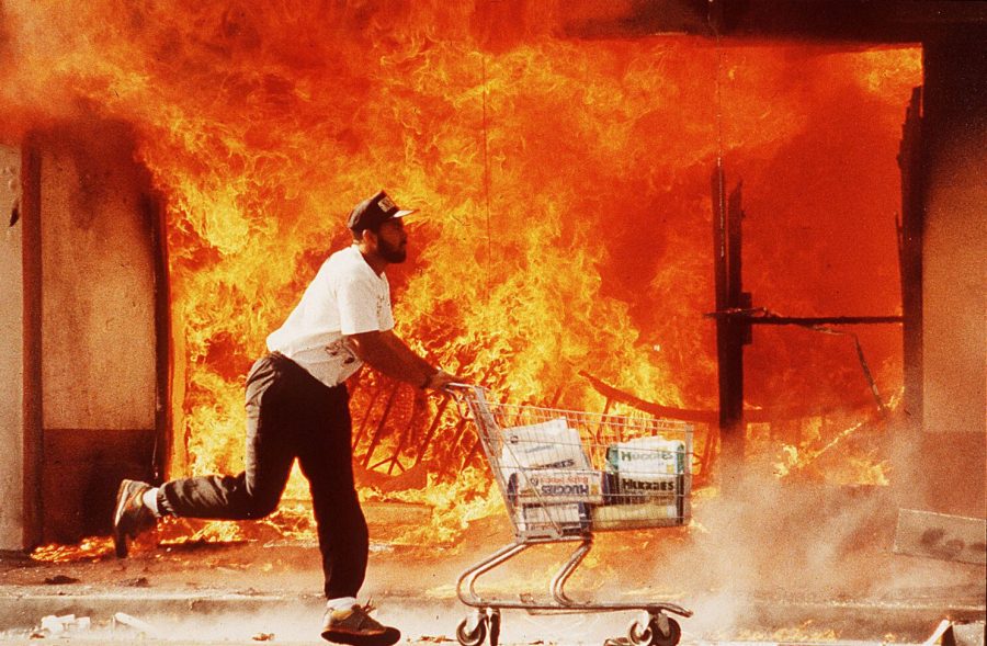 Man pushing shopping cart in front of flames.
